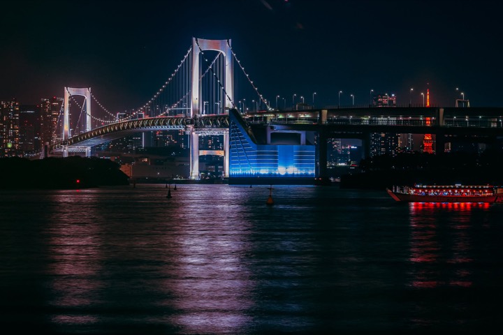 Rainbow Bridge illuminated at night over Tokyo Bay with a yakatabune boat, seen from Odaiba
